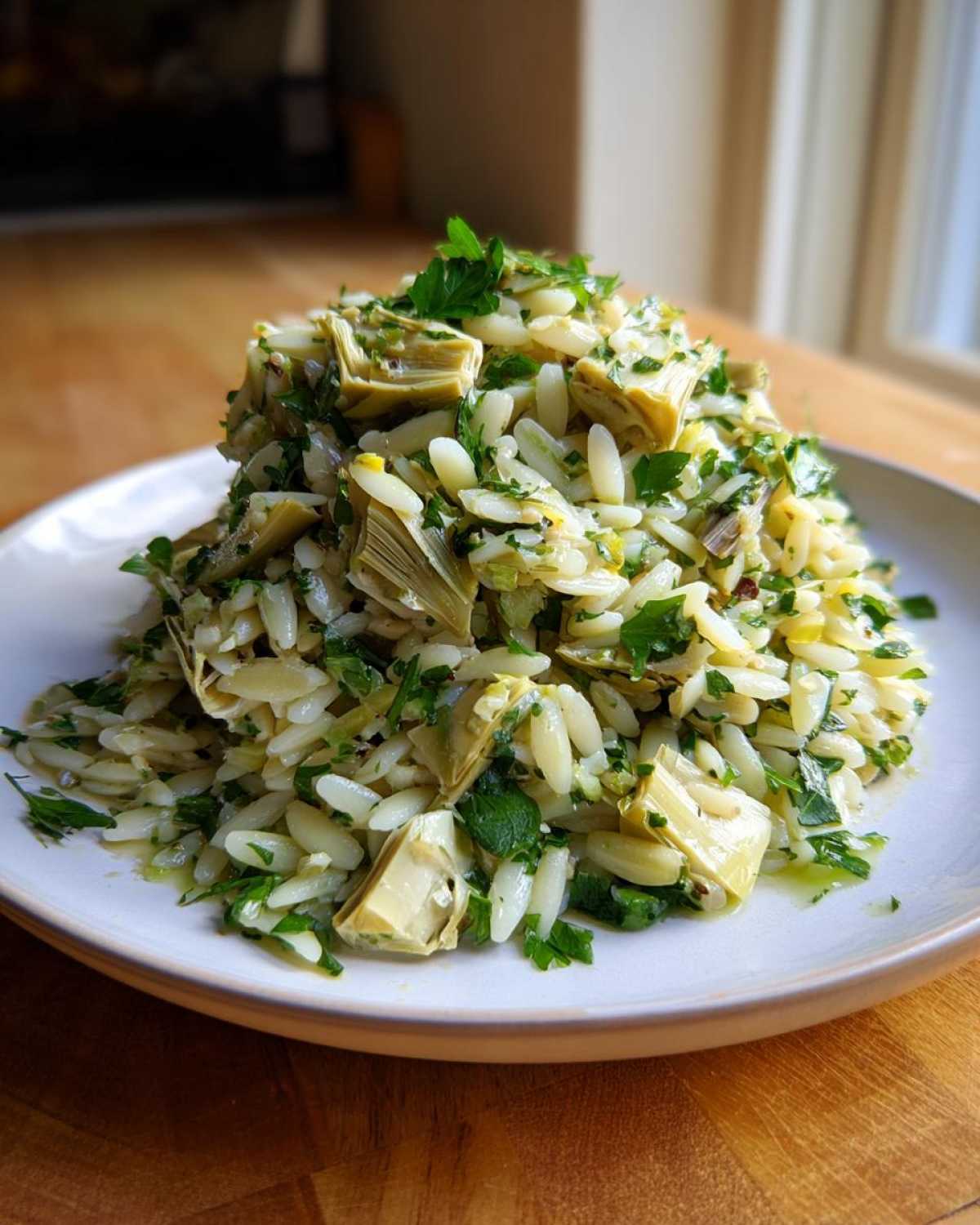 A mound of Artichoke Lemon Orzo Salad featuring orzo pasta, artichoke hearts, and fresh parsley, served on a light plate.