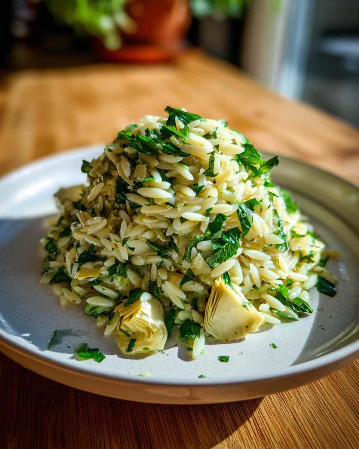 A mound of Artichoke Lemon Orzo Salad mixed with bright green herbs, served on a light gray plate.