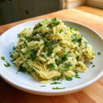 A close-up of a white bowl filled with Artichoke Lemon Orzo Salad, topped generously with fresh chopped parsley.