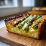 A thick slice of golden-brown Asparagus Gruyere Quiche showing the creamy filling and bright green asparagus spears.
