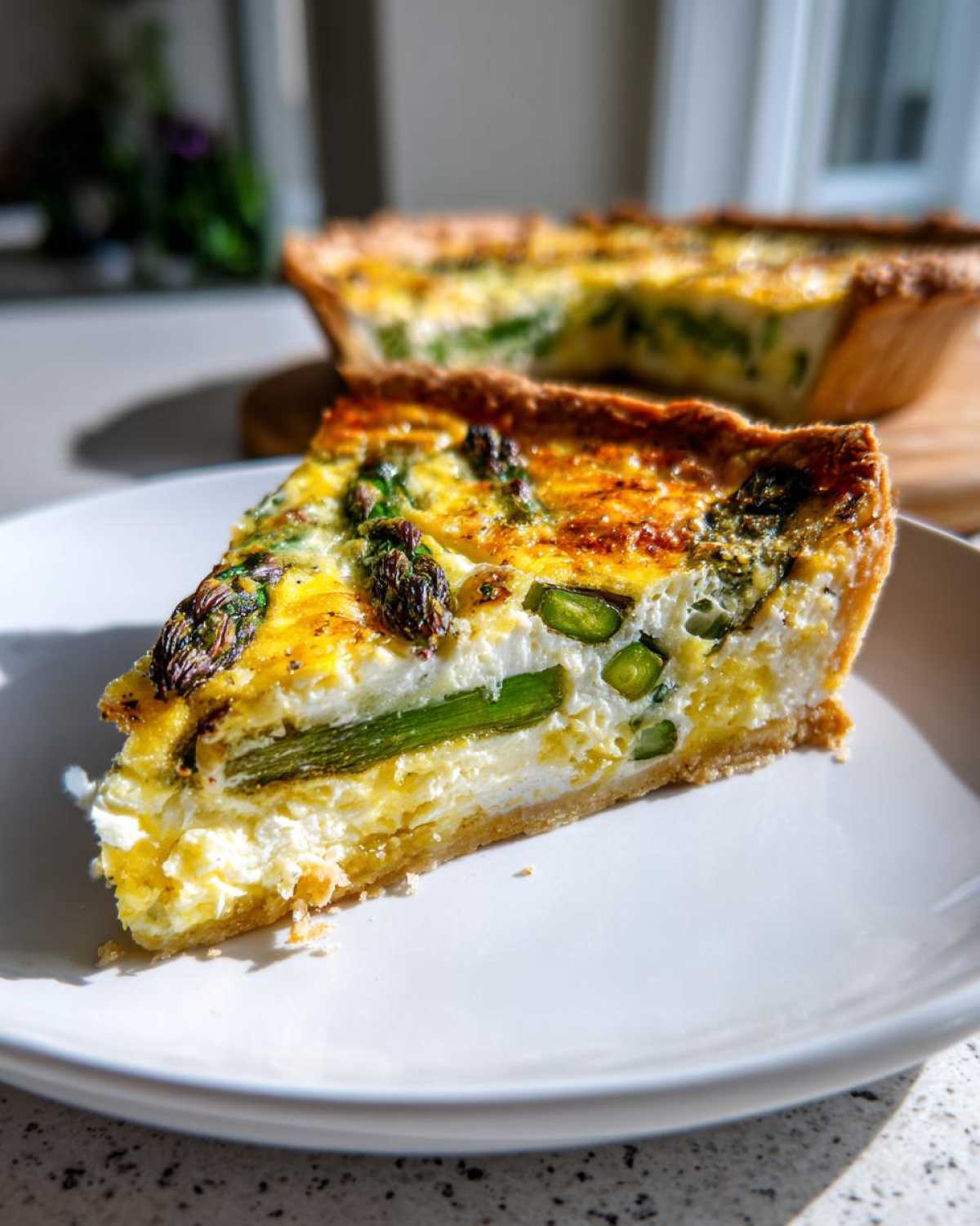 A close-up slice of golden-brown Asparagus Gruyere Quiche with visible asparagus spears on a white plate.
