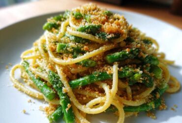A close-up of a serving of Asparagus Lemon Pasta with Parmesan Crumbs, featuring bright green asparagus spears mixed with pasta.