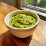 A close-up of vibrant green Avocado Tomatillo Salsa Verde, thick and textured, served in a small white bowl on a wooden surface.