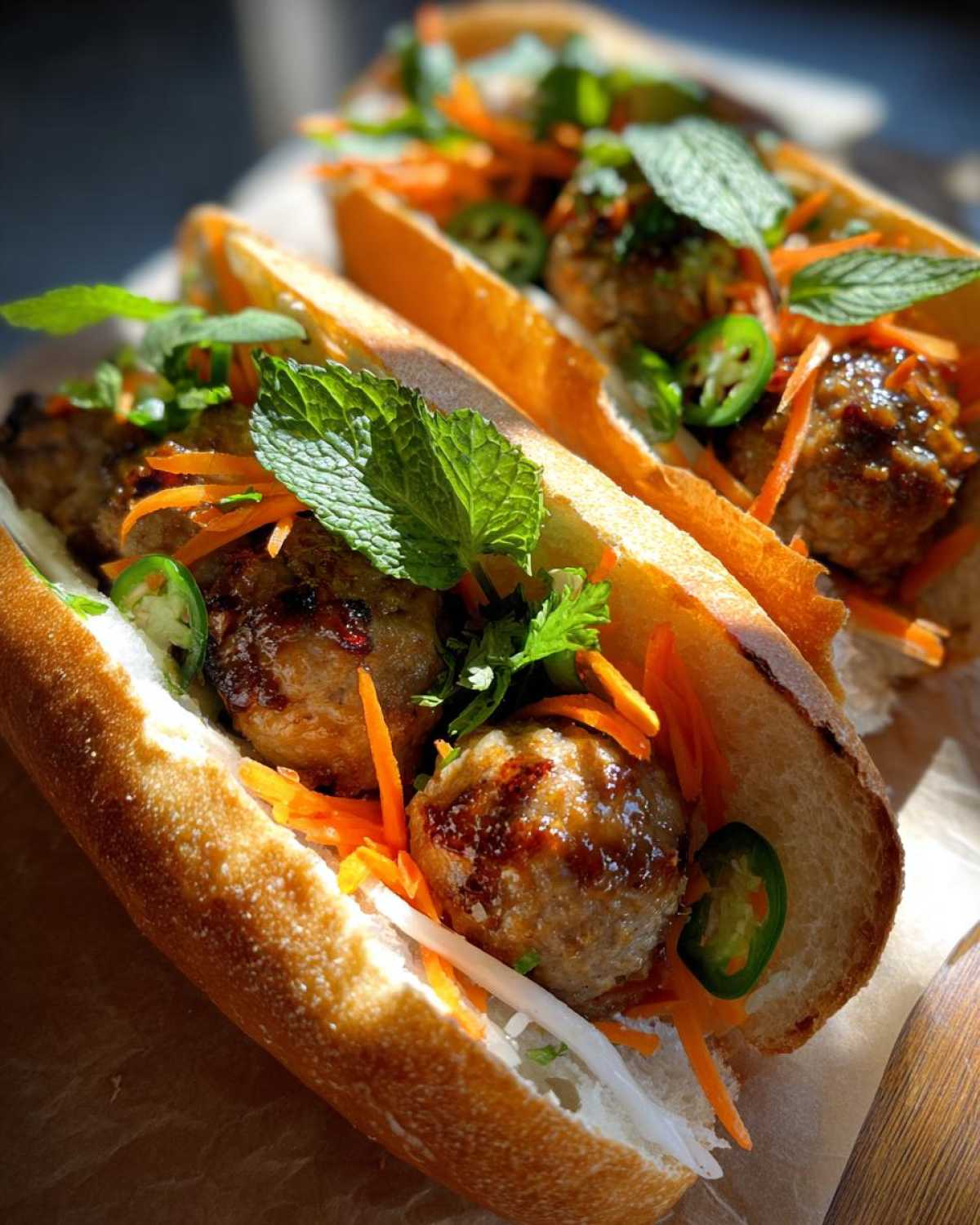 Two delicious Banh Mi Meatball Subs filled with glazed meatballs, pickled carrots, jalapenos, and fresh mint.