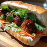 A close-up of a delicious Banh Mi Meatball Subs sandwich filled with glazed meatballs, pickled carrots, daikon, and fresh mint.