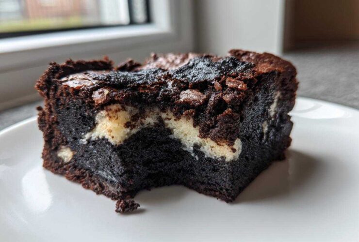 A rich, dark square of Black Sesame Mochi Brownies with a chewy texture and white swirls, served on a white plate.
