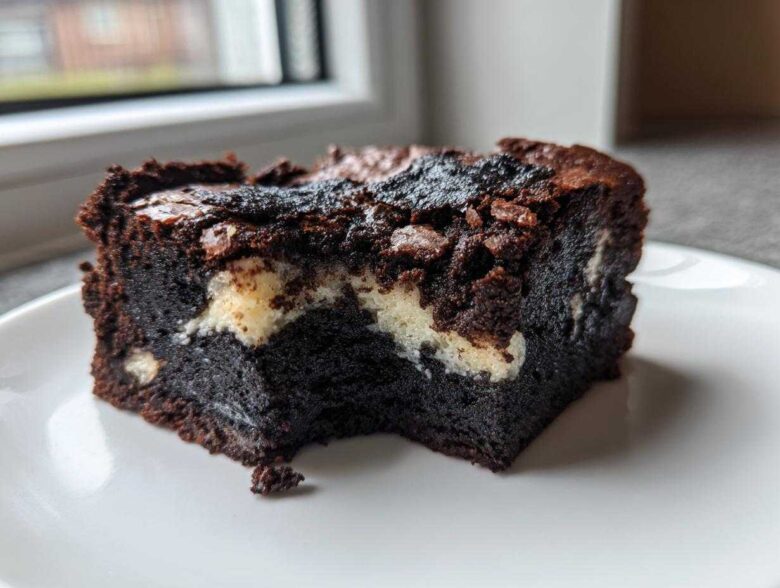 A rich, dark square of Black Sesame Mochi Brownies with a chewy texture and white swirls, served on a white plate.
