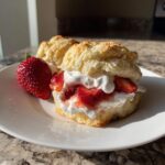 A fluffy biscuit split and filled with whipped cream and macerated strawberries, served as Breakfast Strawberry Shortcakes with Quick Jam.