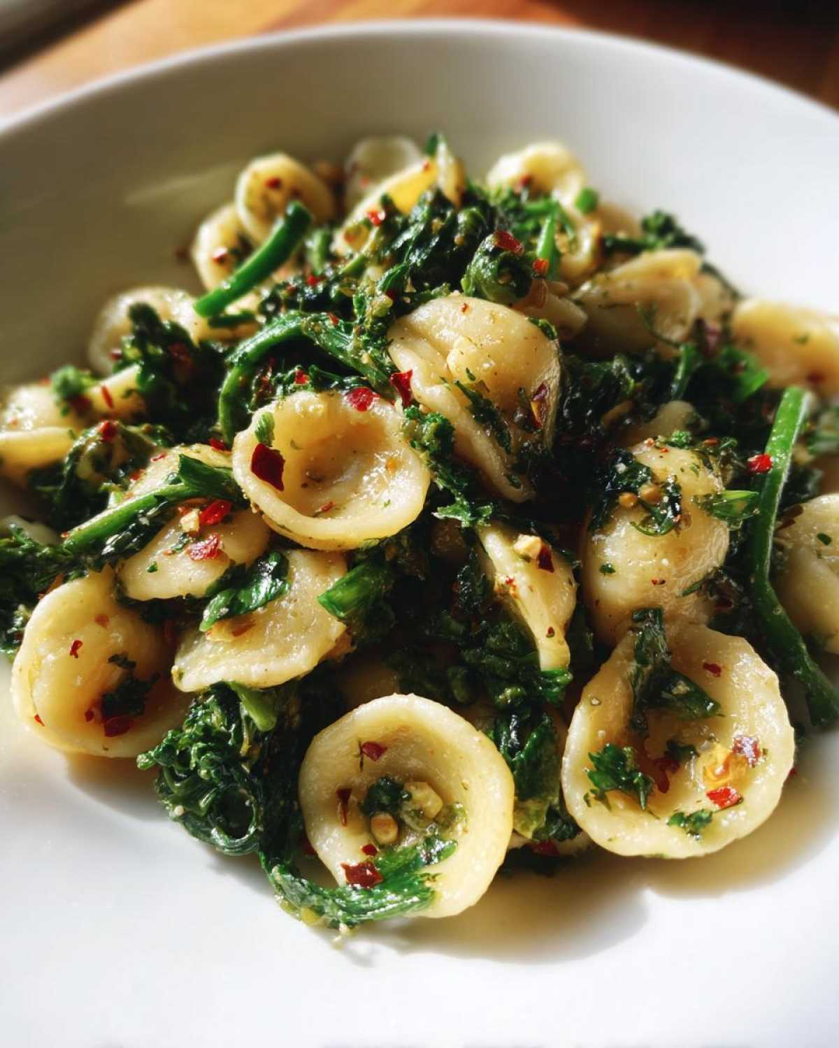 Close-up of orecchiette pasta tossed with vibrant green broccoli raab and red chili flakes.