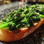 A close-up, sunlit shot of a single slice of Broccolini Garlic Anchovy Toast featuring bright green broccolini on toasted bread.