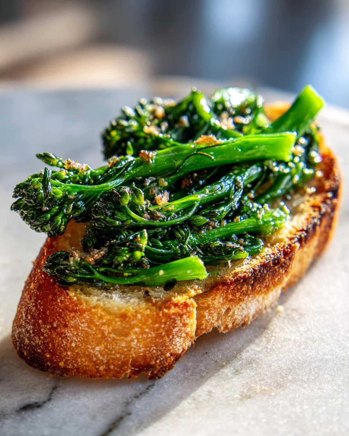 A single piece of toasted bread topped generously with bright green, sautéed broccolini garlic anchovy toast mixture.