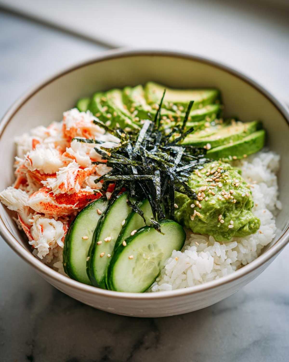 A close-up of a California Sushi Bowl with Crab, featuring shredded crab meat, sliced avocado, cucumber, and mashed avocado over rice.