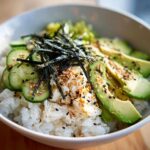 Close-up of a California Sushi Bowl with Crab served over white rice, topped with sliced avocado, cucumber, nori, and sesame seeds.