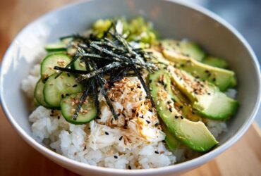 Close-up of a California Sushi Bowl with Crab served over white rice, topped with sliced avocado, cucumber, nori, and sesame seeds.