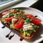 A slice of Caprese Avocado Toast topped with mashed avocado, mozzarella, tomatoes, basil, and balsamic drizzle.