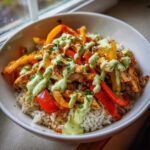 A close-up of a Charred Pepper Fajita Bowl featuring seasoned chicken, colorful charred peppers over rice, drizzled with a vibrant green sauce.