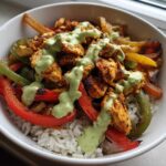 Close-up of a Charred Pepper Fajita Bowl featuring seasoned chicken, charred peppers, and white rice topped with a green creamy sauce.