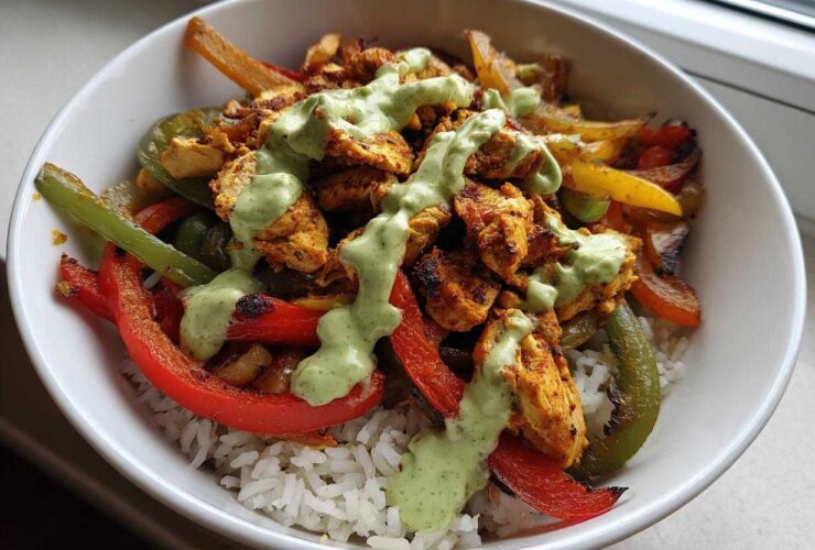 Close-up of a Charred Pepper Fajita Bowl featuring seasoned chicken, charred peppers, and white rice topped with a green creamy sauce.