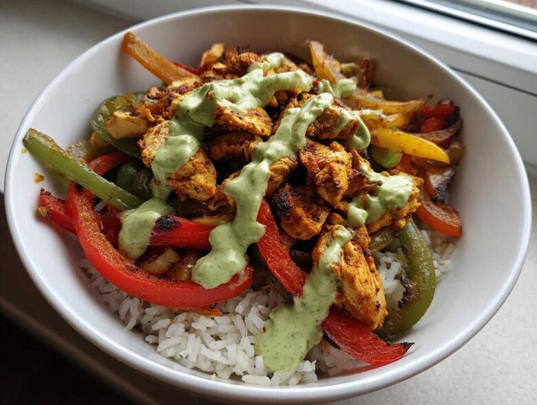 Close-up of a Charred Pepper Fajita Bowl featuring seasoned chicken, charred peppers, and white rice topped with a green creamy sauce.