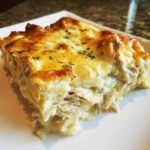 A close-up slice of Cheesy Chicken Enchilada Bake showing shredded chicken layers and a bubbly, golden-brown cheese topping.