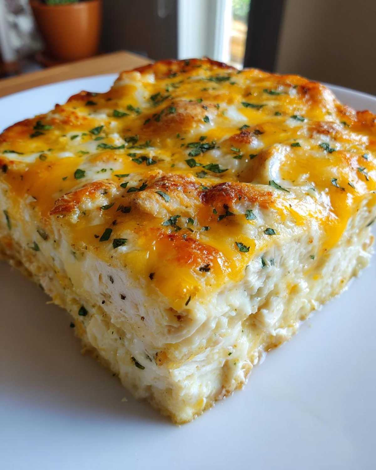 Close-up of a square slice of Cheesy Chicken Enchilada Bake, showing layers of creamy filling and a golden, bubbly cheddar cheese topping.