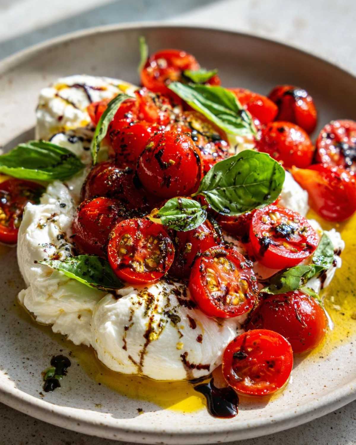 A serving of Cherry Tomato Burrata Caprese featuring creamy burrata topped with roasted cherry tomatoes, basil, and balsamic glaze.