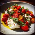 Close-up of a vibrant Cherry Tomato Burrata Caprese drizzled with balsamic glaze and fresh basil.