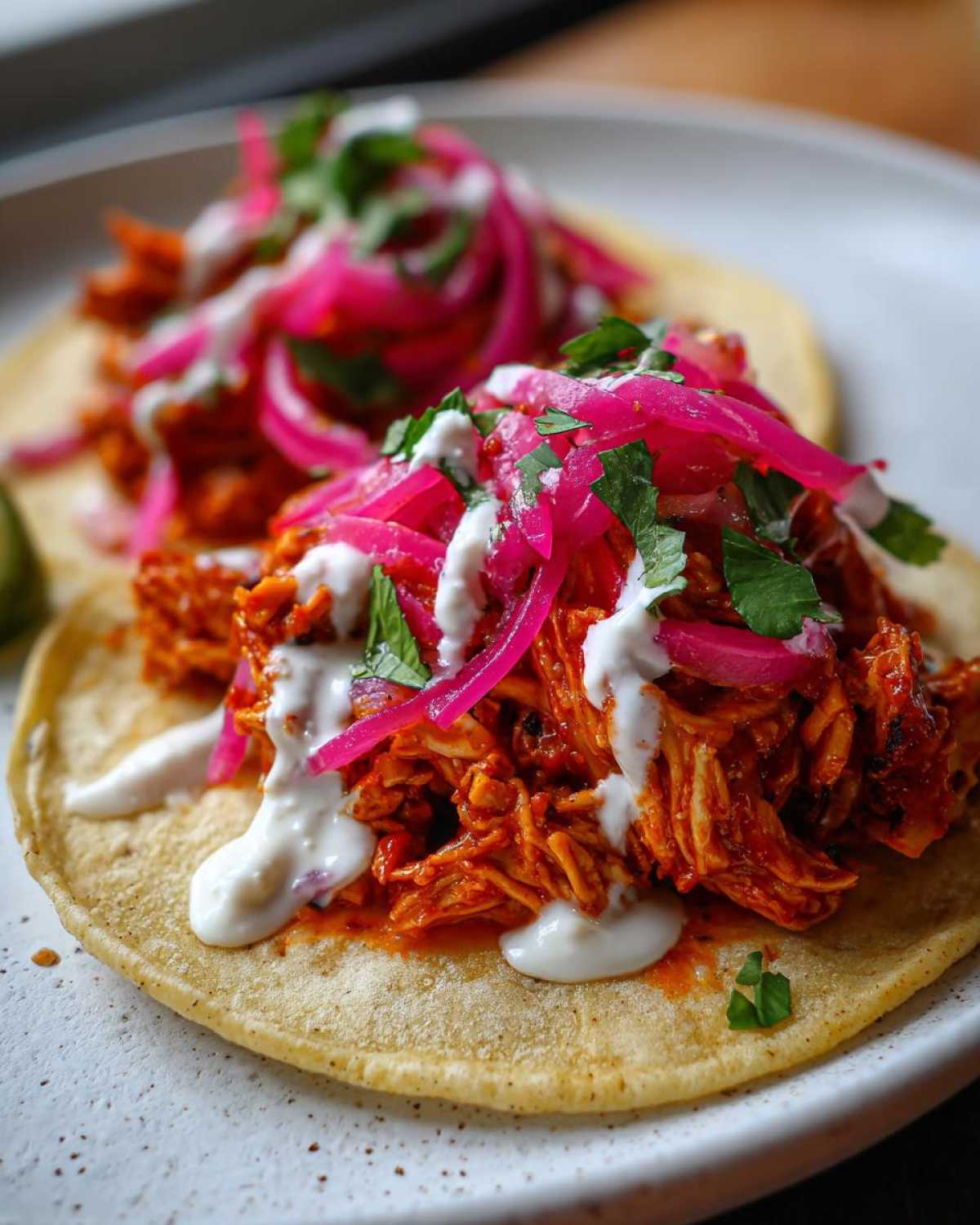 Two delicious Chicken Tinga Tostadas topped with vibrant pickled onions, crema, and cilantro on a white plate.