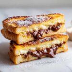 Two halves of Chocolate Chip Brioche Toast stacked, showing melted chocolate filling oozing out, dusted with powdered sugar.