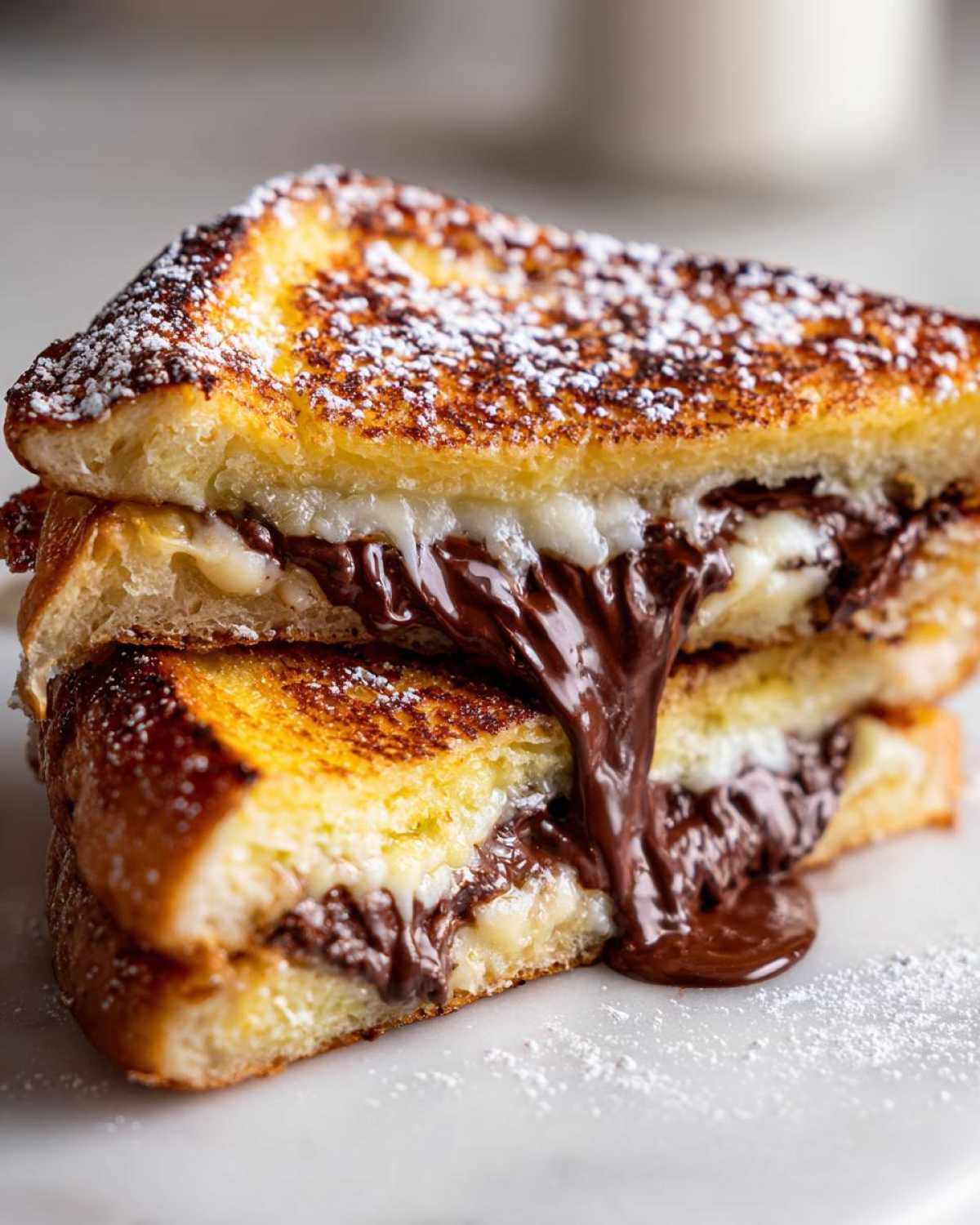 Two halves of golden-brown Chocolate Chip Brioche Toast stacked, revealing melted chocolate oozing out, dusted with powdered sugar.