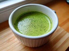 Close-up of vibrant green Cilantro Lime Crema with fine bubbles in a white bowl, sitting on a wooden surface.
