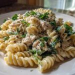 A close-up of Cold Chicken Caesar Pasta Salad featuring rotini pasta, shredded chicken, greens, and Parmesan cheese.