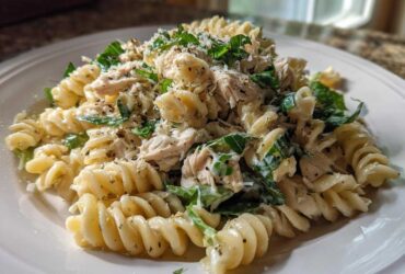A close-up of Cold Chicken Caesar Pasta Salad featuring rotini pasta, shredded chicken, greens, and Parmesan cheese.