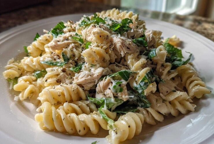 A close-up of Cold Chicken Caesar Pasta Salad featuring rotini pasta, shredded chicken, greens, and Parmesan cheese.