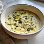 A close-up of creamy Roasted Garlic White Bean Soup, drizzled with olive oil and topped with fresh parsley.