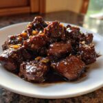 Close-up of tender, dark, glazed pieces of Filipino Chicken Adobo served on a white plate.
