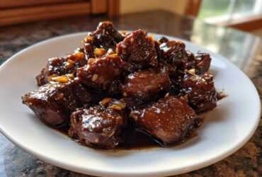 Close-up of tender, dark, glazed pieces of Filipino Chicken Adobo served on a white plate.