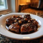 Close-up of tender pieces of Filipino Chicken Adobo coated in a rich, dark sauce with whole cloves of garlic and peppercorns.