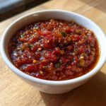 A close-up of chunky, deep red Fire-Roasted Tomato Salsa Roja served in a small white bowl on a wooden surface.