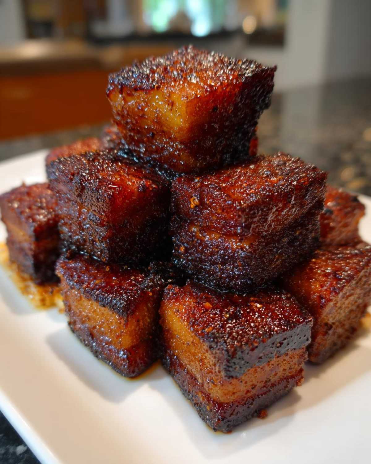 Close-up of a stack of perfectly caramelized Five-Spice Pork Belly Bites on a white plate.