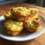 Five golden brown Garden Herb Egg Muffins piled on a small white plate, sprinkled with green herbs.