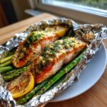 Two perfectly cooked Garlic Dijon Salmon Packets served over bright green asparagus with charred lemon slices.