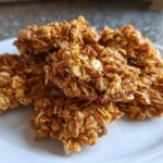 A pile of sticky, golden Maple Pecan Granola Clusters made with oats and coated in a sweet glaze, served on a white plate.