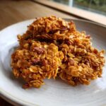 Close-up of several golden Maple Pecan Granola Clusters piled on a light ceramic plate.