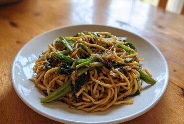A white plate holding a generous serving of glossy Ginger Scallion Noodles mixed with bright green scallions.