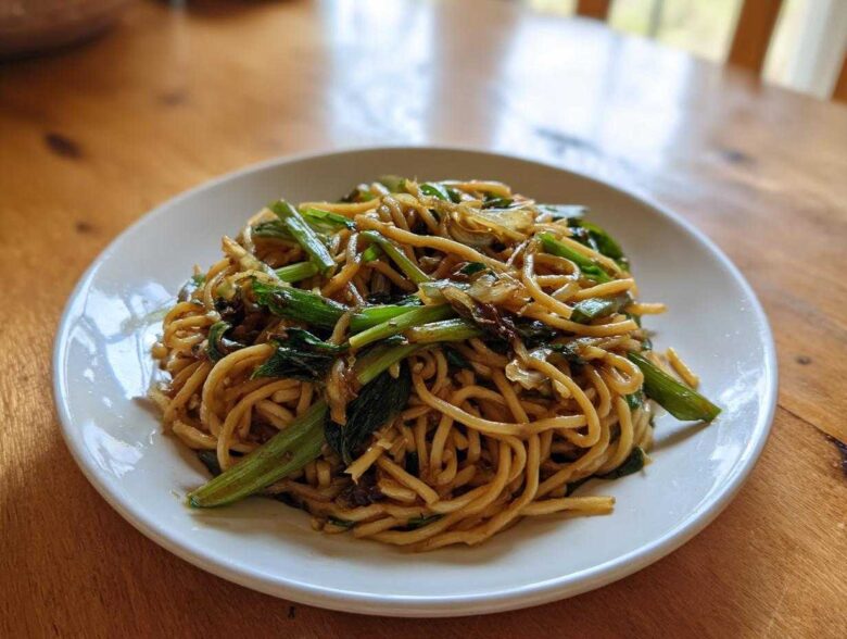 A white plate holding a generous serving of glossy Ginger Scallion Noodles mixed with bright green scallions.
