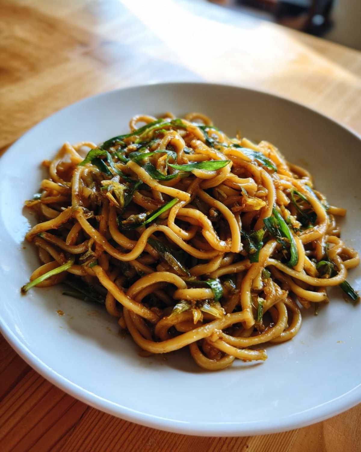 A close-up of thick, glossy noodles coated in sauce and mixed with bright green scallions, representing Ginger Scallion Noodles.