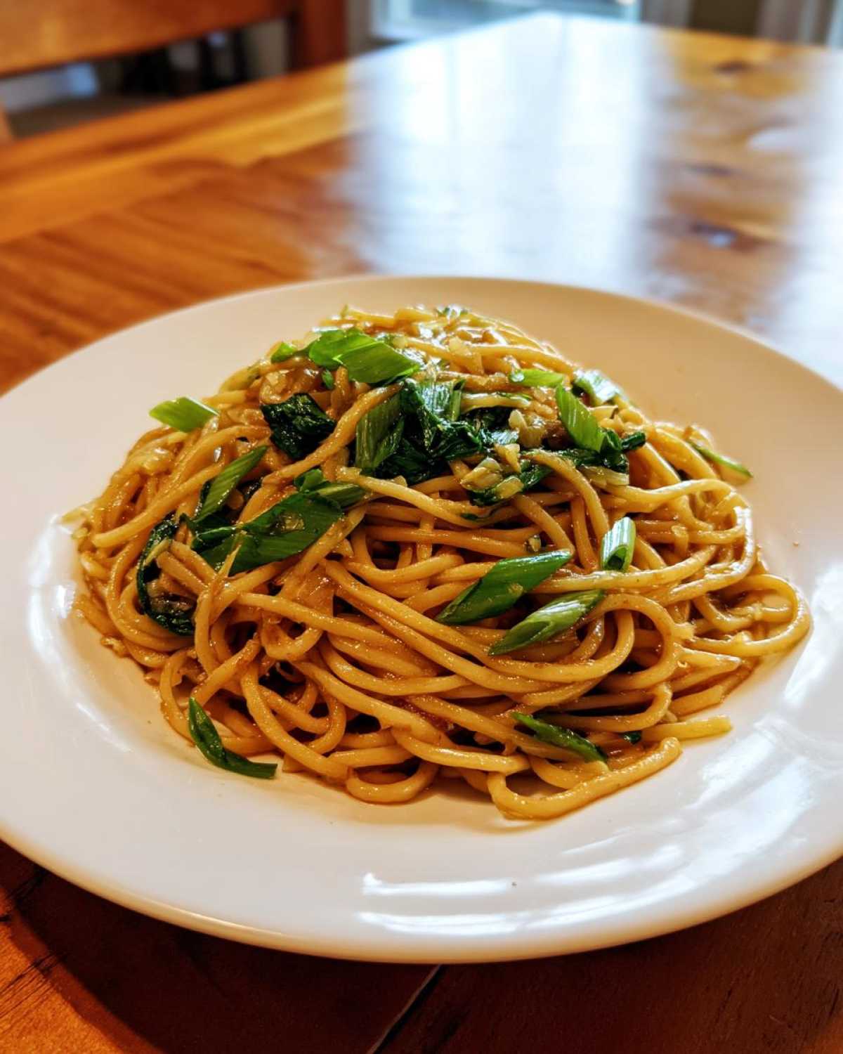 A close-up of a white plate piled high with glistening Ginger Scallion Noodles topped with fresh green scallions.