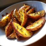 Close-up of crispy, golden Greek Lemon Potatoes with Oregano wedges served in a white bowl.