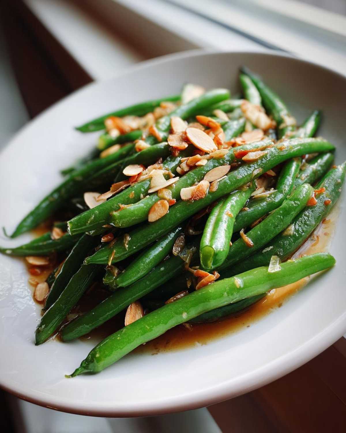 Close-up of bright green beans tossed in brown butter sauce and topped with toasted sliced almonds: Green Bean Almondine with Brown Butter.
